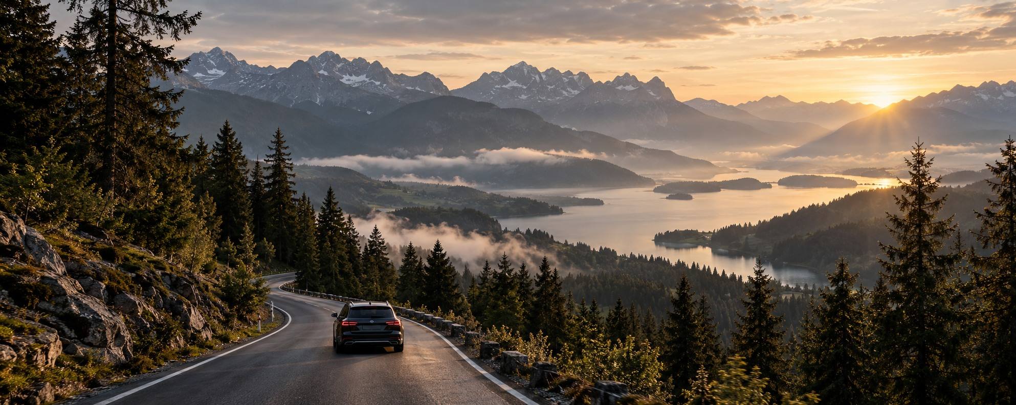 Ein dunkler Kombi fährt auf einer leeren Straße durch nebligen Kiefernwald auf einen See zu